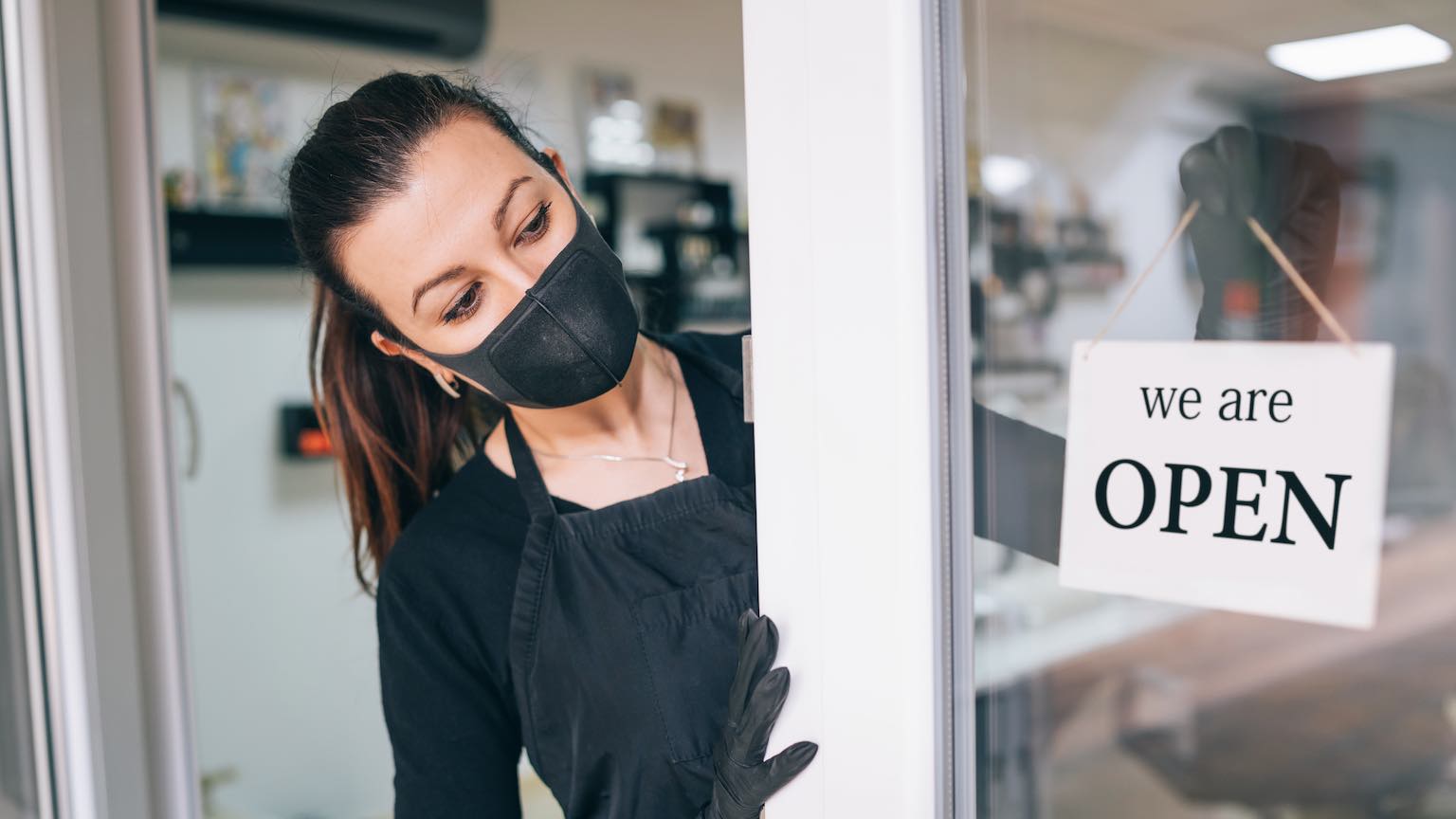 Happy business owner hanging an open sign during COVID-19