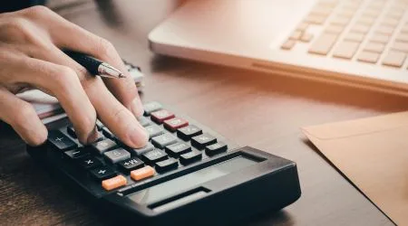 Hand on a calculator near a laptop