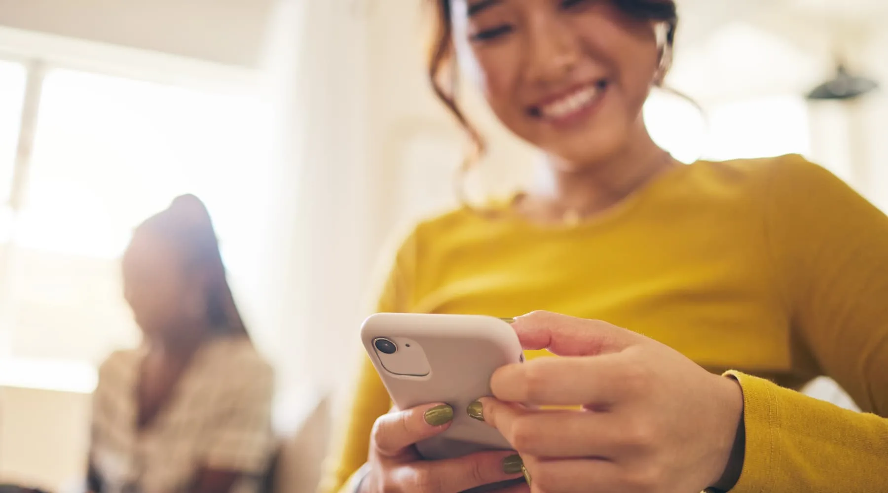 Woman with a yellow sweater and green fingernails holding a phone