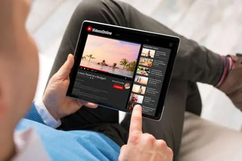 An over-the-shoulder view of a person using a tablet to watch a video on an online platform