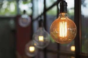 A close-up, shallow-depth-of-field shot of several decorative Edison-style light bulbs hanging and glowing with warm orange light against a blurred background.
