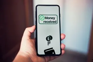 A hand holding a smartphone showing a "Money received" confirmation screen with a green checkmark icon.