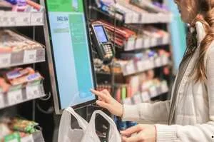 A close-up of a person using a smartphone to make a contactless payment at a grocery store card reader.