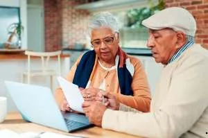 An older man and woman walking together on a sunny path in a park, smiling and laughing.