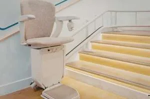A motorized chair lift for seniors installed on a wooden staircase with lit steps, providing accessibility to the upper floor of a home.