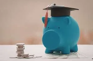 A graduation cap and a diploma tied with a red ribbon resting on several stacks of coins, symbolizing education funding and student grants.