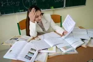 A stressed student sits at a desk with their head in their hands, surrounded by messy stacks of papers, textbooks, and a laptop, illustrating an overwhelming study load.