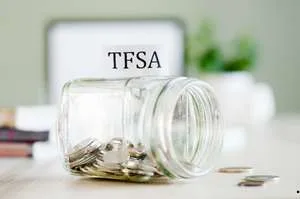 A glass jar lying on its side on a desk, filled with coins, with a "TFSA" label attached.