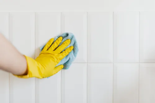 Picture or a person cleaning white tiles with a cloth