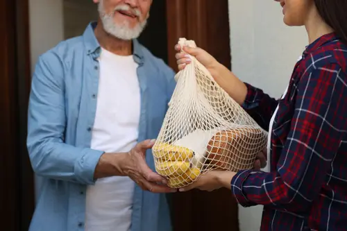 Woman holding out a bag of groceries to an older man