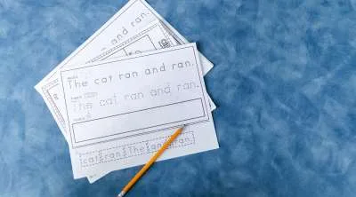 Educational tracing worksheets for children featuring the sentence "The cat ran and ran" laid out on a blue textured surface with a pencil.