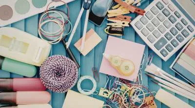 A top-down view of a bright workspace filled with colorful crafting materials, including spools of thread, buttons, ribbons, and scissors.