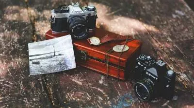 An aesthetic arrangement of antique items on a wooden table, including an old-fashioned clock and two vintage cameras.
